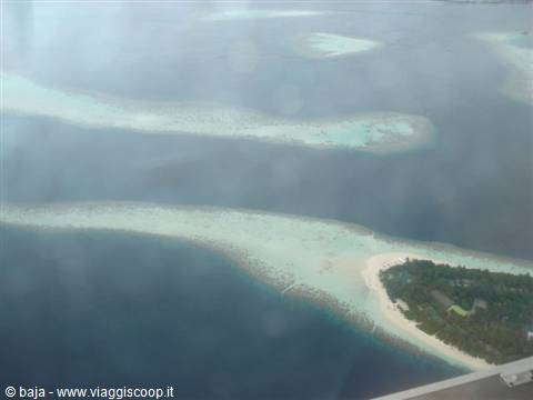 Coral island with white beach and turquoise lagoon seen from the plane