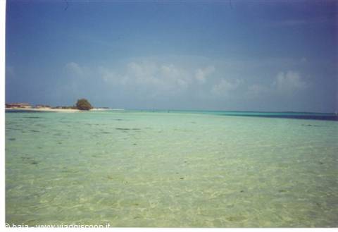 Clear turquoise water over white sand beach, blue sky with clouds