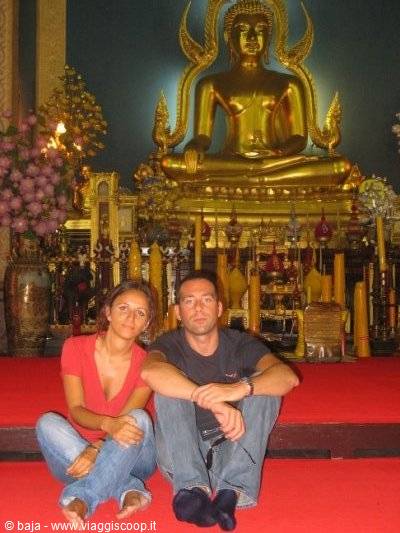 Couple sitting on red carpet in front of a golden Buddha inside a temple
