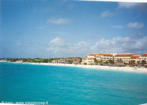 White sand beach in front of terracotta-roofed resorts, turquoise sea