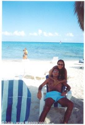 Woman hugs man on beach chair under striped umbrella, Caribbean sand and turquoise sea