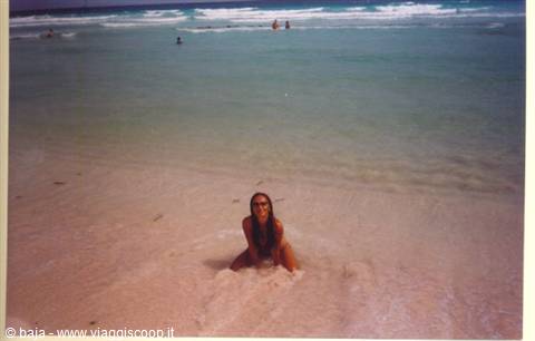 Woman kneeling in sea foam on pale sand, tropical beach