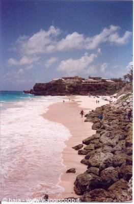 Pink sand beach with rocky shore, swimmers and cliffside hotel under cloudy sky