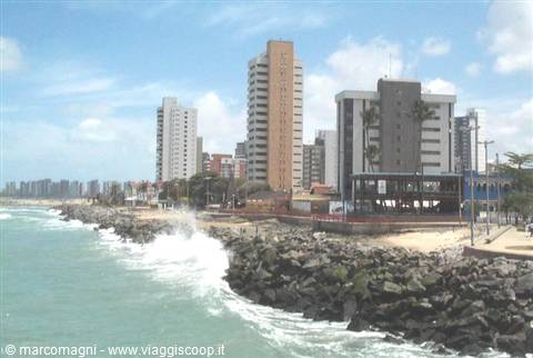 Beachfront high-rises, waves crashing on dark breakwater rocks