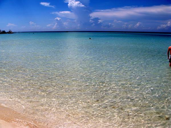 Clear turquoise water over sandy beach, a swimmer under white clouds