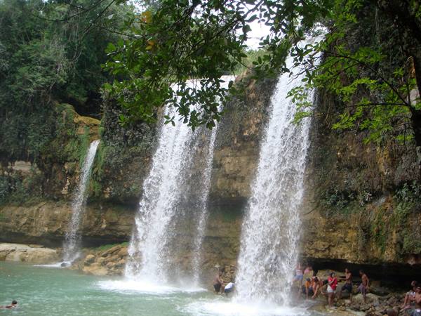 Waterfalls pouring over limestone cliffs, swimmers on the green shore