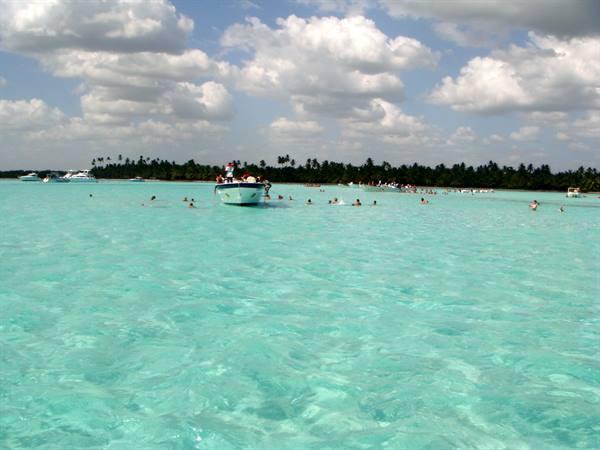 Swimmers in turquoise water with boat and palms in background