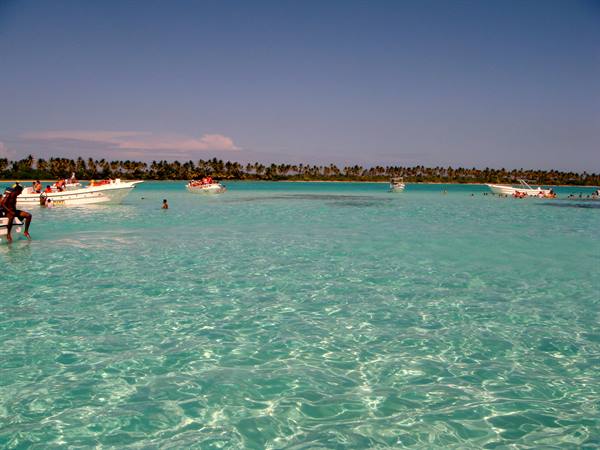 White boats anchored in clear turquoise water, swimmers and palms along the shore