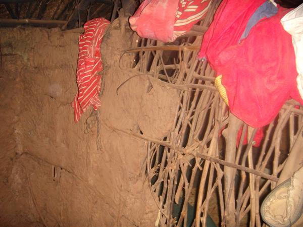 Mud wall with woven branches inside a rural hut, red clothes hanging