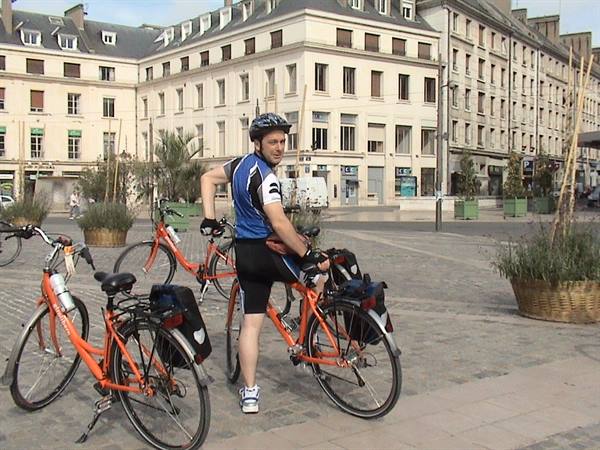 Cyclist in helmet beside two orange bicycles on a square with historic buildings