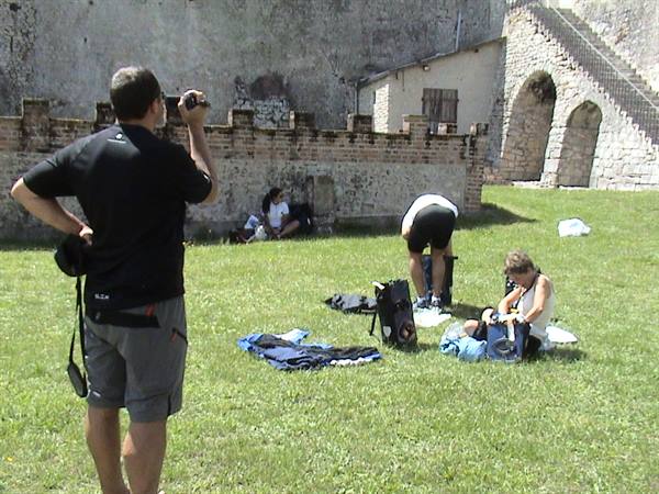 Tourists photographing and resting on the grass by old stone fortress walls
