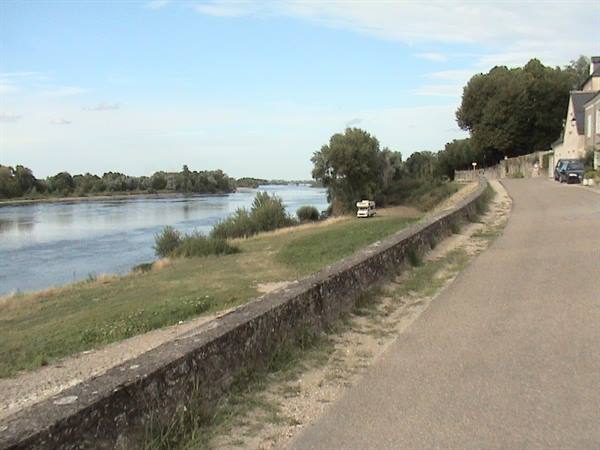 Stone embankment along a wide river, paved road and houses among trees