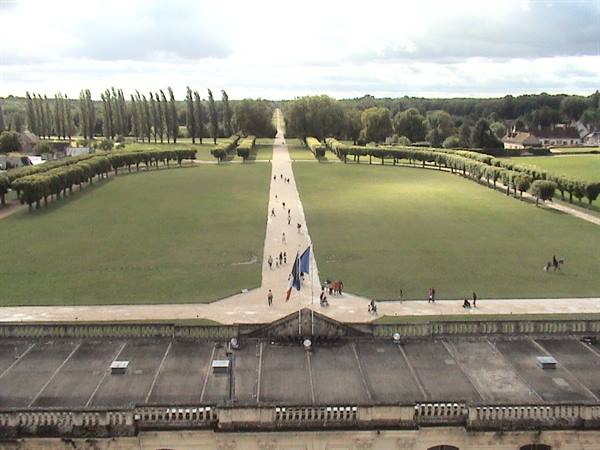 Straight gravel path between lawns and clipped hedges, slate roofs and French flag