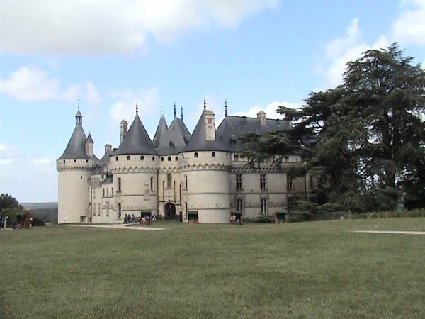 Chaumont castle: stone towers with cone roofs, green lawn, cloudy sky