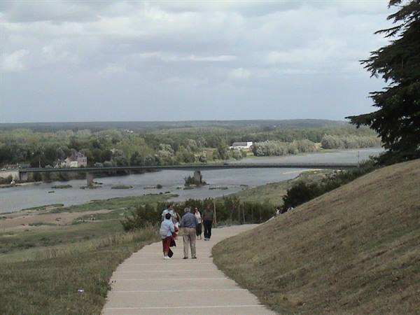 Visitors walking paved path down toward river with long bridge