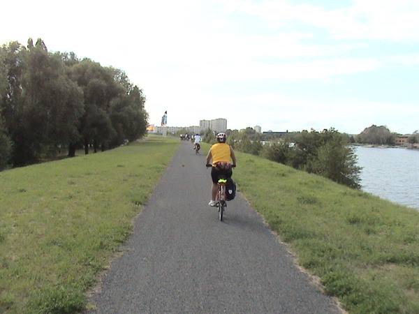 Cyclist in yellow jersey rides paved path beside the river