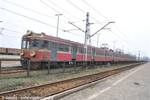 Vintage red train departing on tracks beneath the electric wires of the station