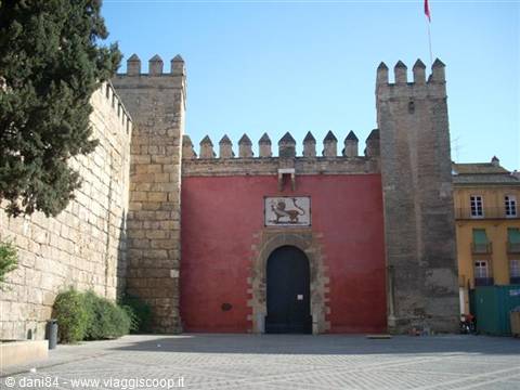 Lion's Gate of Seville's Alcázar, crenellated stone walls and red facade