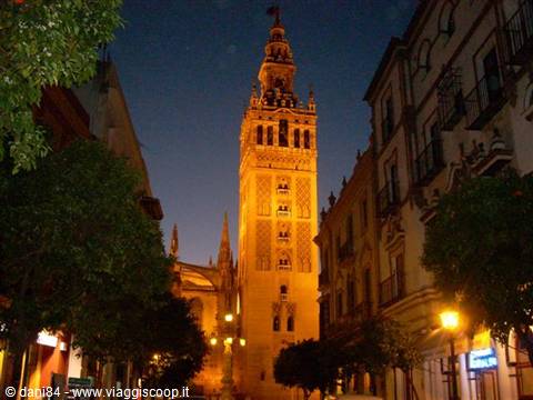 Seville's Giralda tower glowing at night among buildings and street lamps