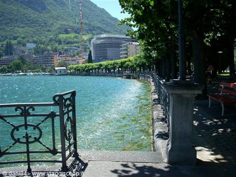 Lugano lakeside promenade, stone parapet, wrought iron railing, shaded benches under trees
