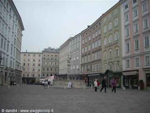 Salzburg, Residenzplatz: baroque fountain among colorful buildings, pedestrians crossing the square