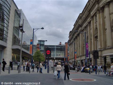 Pedestrians in Exchange Square, Manchester, between modern buildings and stone facades