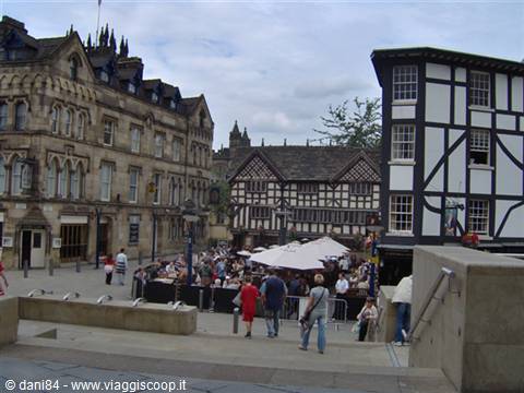 People at outdoor café tables beside old timber-framed buildings in Manchester