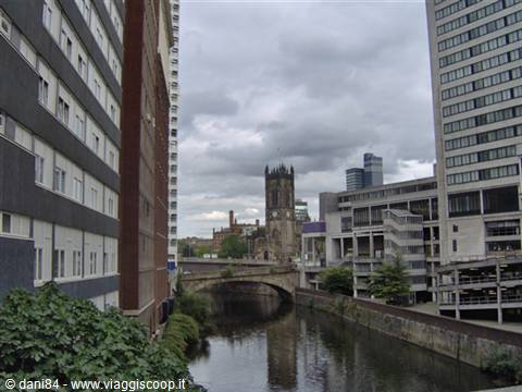 River with stone bridge between modern towers, gothic church tower under grey clouds