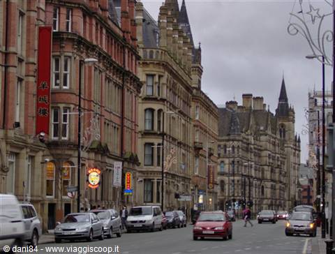 Manchester street with traffic and Victorian brick buildings under grey sky