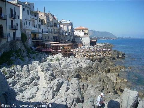 Houses perched on Cefalù rocks, man climbing down to the sea