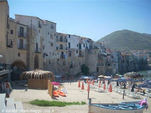 Beach with umbrellas and boats beneath Cefalù old stone houses