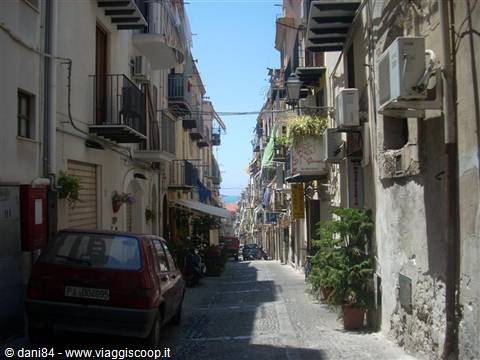 Narrow alley with houses, iron balconies, parked car and green plants