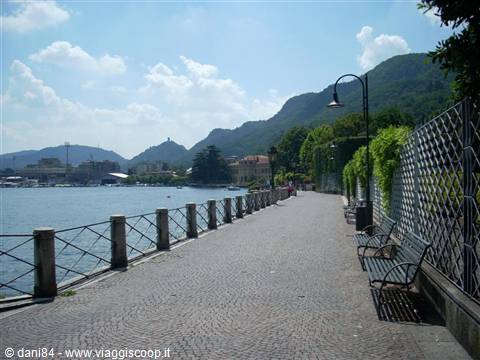 Paved lakeside promenade with wrought iron benches, lamp post and mountains behind