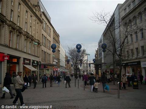 Pedestrian shopping street with blue decorative spheres, people walking among stone buildings
