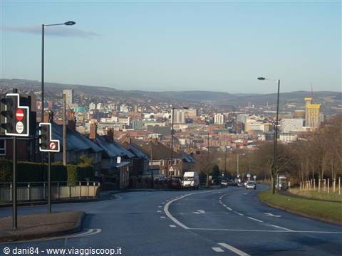 Road descending toward Sheffield with traffic lights, brick houses and hills behind