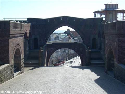 Red brick arches with stairs and a bridge, framing a city street below
