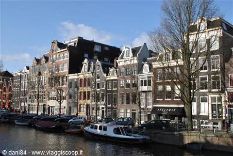 Narrow gabled houses along the canal, moored boats, blue sky