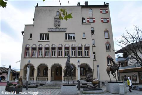 Town hall with painted crest and bronze horse sculptures under grey sky
