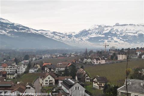 Rooftops and houses of Vaduz beneath snowy mountains, grey sky