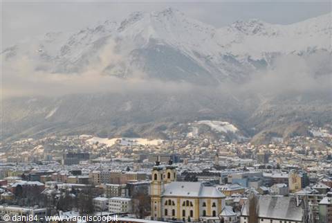 Innsbruck: yellow baroque church among snow-covered rooftops, foggy alpine peaks