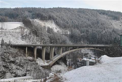 Concrete arch bridge spans the snowy valley among snow-covered forested hills