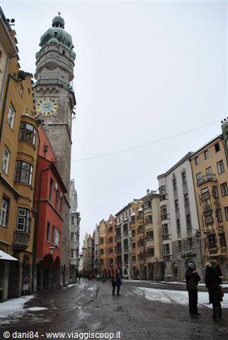 Clock tower over colorful houses in Innsbruck, wet snow on street