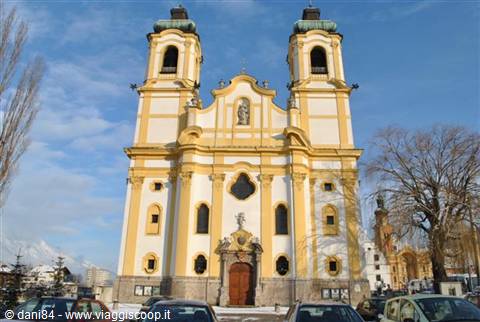 Yellow and white baroque church with two towers, parked cars, Innsbruck