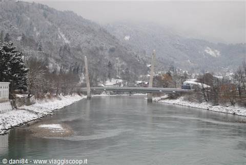 Snow-covered cable-stayed bridge over the river, white frosted woods