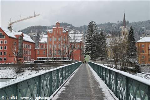 Snow-covered green footbridge, red buildings and church spire in background