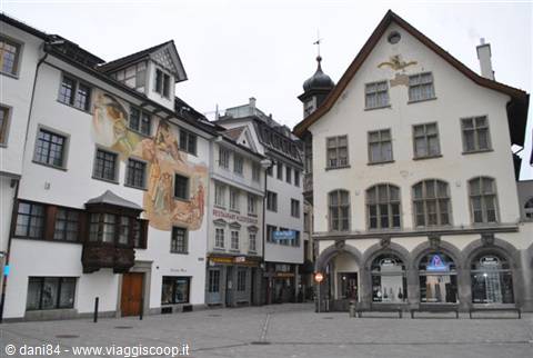 Historic square with white buildings, one frescoed with a wooden oriel window