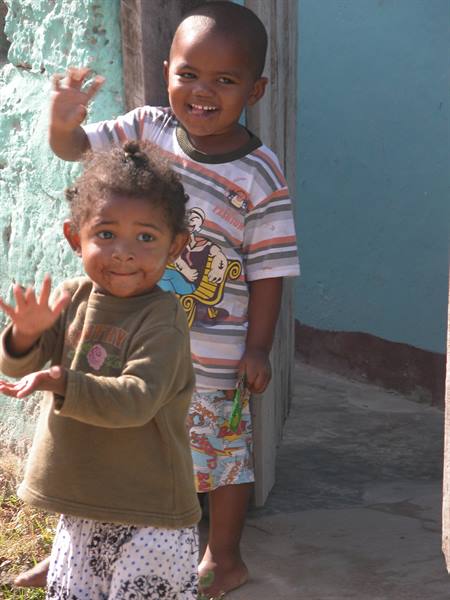 Two smiling children waving in front of a blue wall