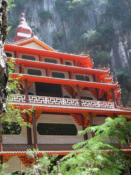 Multi-tiered Buddhist temple with red roofs built against a limestone cliff