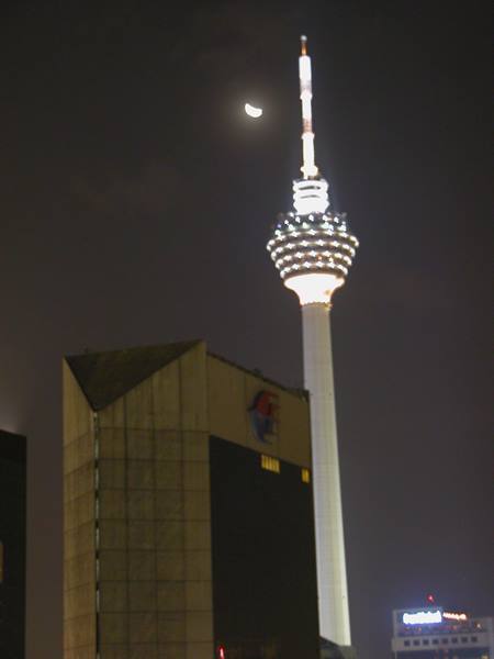 Kuala Lumpur Tower lit at night with crescent moon above buildings