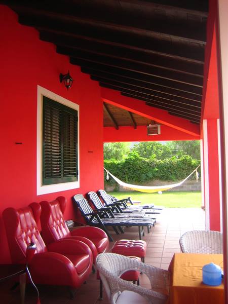 Red veranda with leather armchairs, sun loungers and hammock on the lawn
